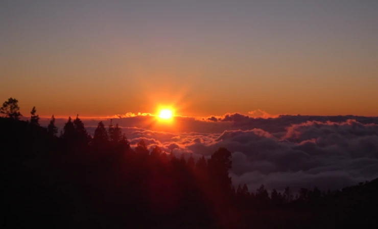 The viewer is above the cloud cover. The sun is just setting behind the clouds.